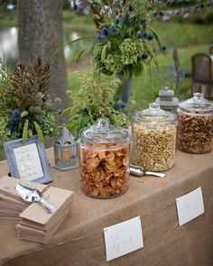 a table topped with jars filled with nuts and other things next to a couple of trees