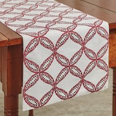 a wooden table topped with a white and red table runner on top of a wooden table