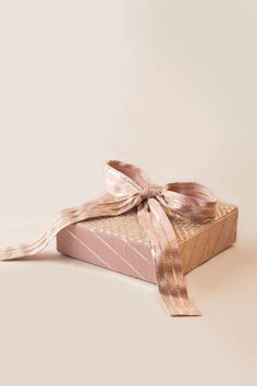 a pink and gold gift box with a ribbon on it's side, against a white background