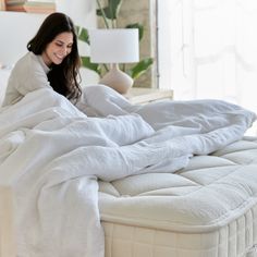 a woman laying on top of a bed covered in white sheets and blankets next to a lamp