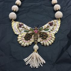 an elaborate necklace with pearls and beads is displayed on a black cloth covered tablecloth