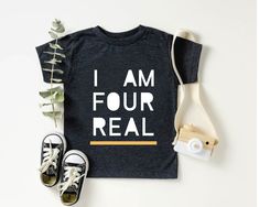 a t - shirt that says i am four real next to sneakers and a plant