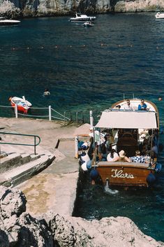 a small boat with people on it in the water near some rocks and other boats