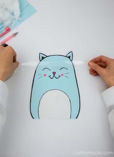 someone is cutting out a paper cutout of a blue cat with pink eyes and whiskers