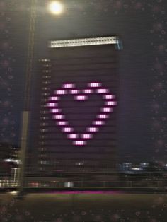 a large building with a neon heart on it's side in front of a full moon