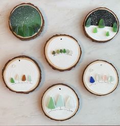 four pieces of wood with small trees painted on them and snow covered ground in the background