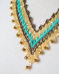 the beaded necklace is hanging on the white fabric with gold and blue beads around it