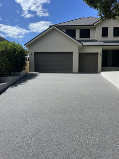 an empty driveway in front of a house with two garages and trees on both sides