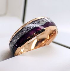 a wedding ring with purple and white stones on it's side, sitting on a table