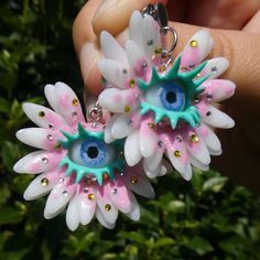 two white and pink flowers with blue eyes are being held by someone's hand