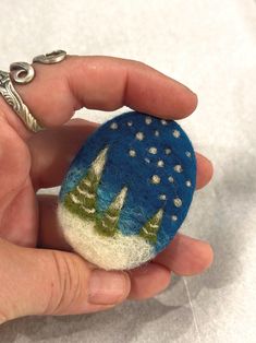 a hand holding a small felt ornament in the shape of a night sky with trees