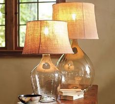 two glass vases sitting on top of a wooden table next to a book and lamp