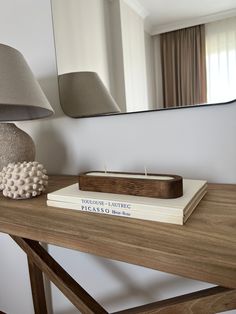 a wooden table topped with books next to a lamp and mirror on top of it