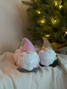 two white and pink gnome figurines sitting next to a christmas tree