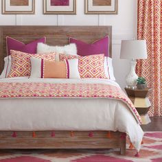 a bed with pink and orange pillows in a bedroom next to two pictures on the wall