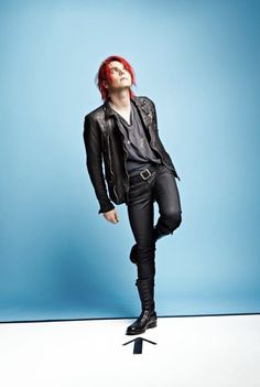 a young man with red hair and black pants posing for a photo in front of a blue background