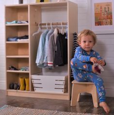 a young child sitting on a stool in front of a closet with clothes and shoes