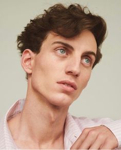 a young man with blue eyes is posing for the camera while wearing a pink shirt