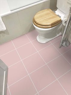 a bathroom with pink floor tiles and a wooden toilet seat in the center of the room