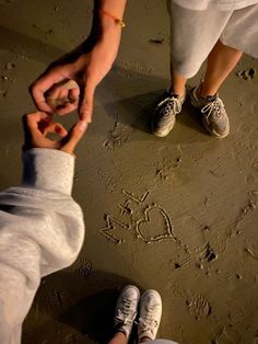 two people holding hands and writing in the sand with hearts drawn on it's side