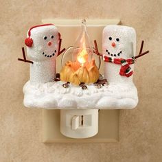 two snowmen sitting next to each other on a light switch cover with a lit candle in the middle