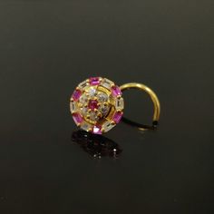 a gold ring with pink and white stones in it on a black surface next to a pair of scissors