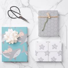 two wrapped gifts on a marble table with scissors and wrapping paper next to each other