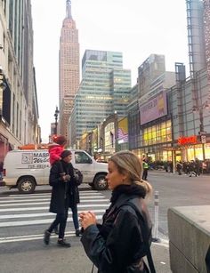 a woman standing on the side of a street next to tall buildings with people walking around