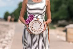 a woman in striped dress holding a white and brown basket with flowers on it's side