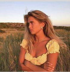 a woman standing in tall grass with her arms crossed and looking off to the side