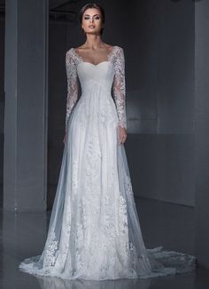 a woman in a white wedding dress with long sleeves and sheer lace on the skirt