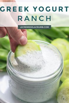 a hand dipping a pickle into a jar of greek yogurt ranch