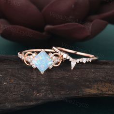 an opal and diamond ring sitting on top of a piece of wood next to a pink flower