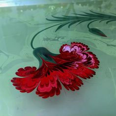 a red flower is floating on top of the glass tablecloth that has been painted with green and pink swirls