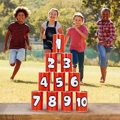 children playing with numbers on an outdoor wooden block set in the grass and smiling at the camera