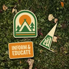 three stickers on the ground with grass and leaves around them, including an information and education sign