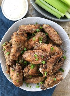 chicken wings with celery and ranch dressing in a white bowl on a blue napkin