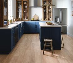 a large kitchen with blue cabinets and wooden floors is pictured in this image, there are stools on the counter