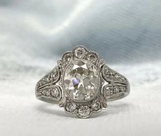 an antique style engagement ring with a large oval cut diamond surrounded by smaller round diamonds