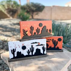 two painted wooden boxes sitting on top of a cement slab next to cactus and trees