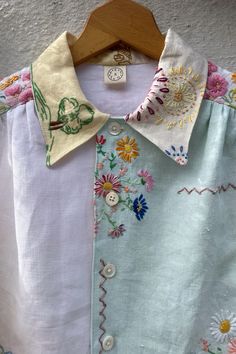 a white shirt with colorful flowers on it and a wooden hanger attached to the collar