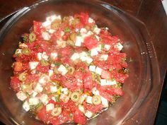 a glass bowl filled with lots of food on top of a wooden table next to a knife