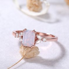 a white opal and diamond ring sitting on top of a rock