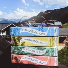 three books stacked on top of each other in front of a house and some mountains