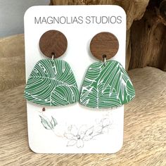 the earrings are made from wood and have green leaves on them, with wooden discs attached to