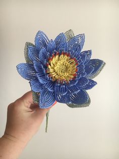 a hand holding a blue flower made out of string and yarn with gold center piece