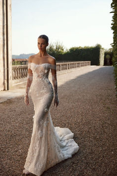 a woman in an off the shoulder wedding dress is standing on a road with her arms behind her back