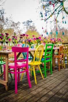 colorful chairs and tables on a deck with flowers in vases hanging from the ceiling