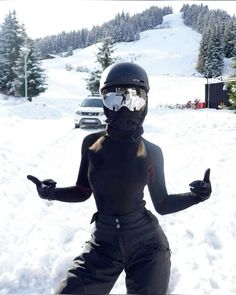 a woman wearing ski goggles standing in the snow with her arms out and thumbs up