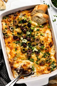 a casserole dish with olives, cheese and bread